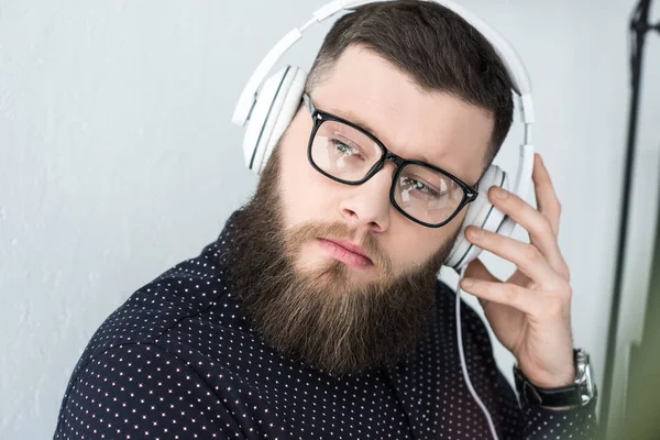 Portrait de l'homme barbu coûteux dans les lunettes écouter de la musique dans les écouteurs — Photo de stock