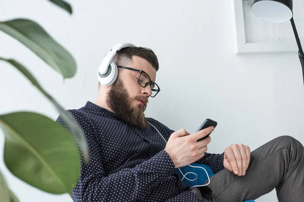Vista lateral del hombre con smartphone escuchando música en auriculares - foto de stock