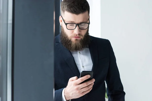 Portrait of focused businessman in eyeglasses using smartphone — Stock Photo