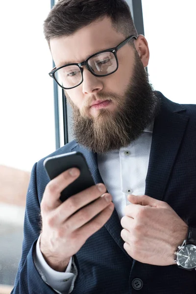 Portrait of focused bearded businessman in eyeglasses using smartphone — Stock Photo