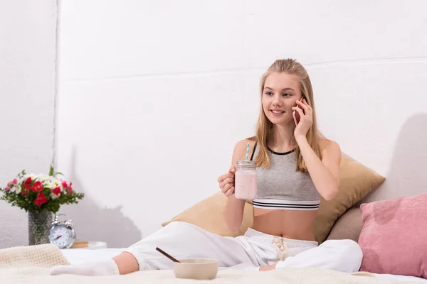 Beautiful young womandrinking milkshake and talking by phone in bed — Stock Photo