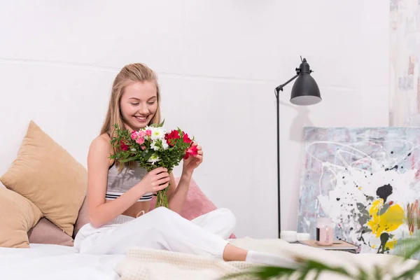 Jolie jeune femme avec beau bouquet assis sur le lit à la maison — Photo de stock