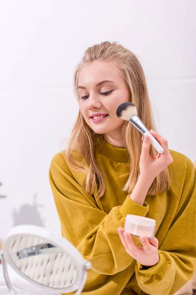 Feliz jovem mulher aplicando blush e olhando para o espelho — Fotografia de Stock