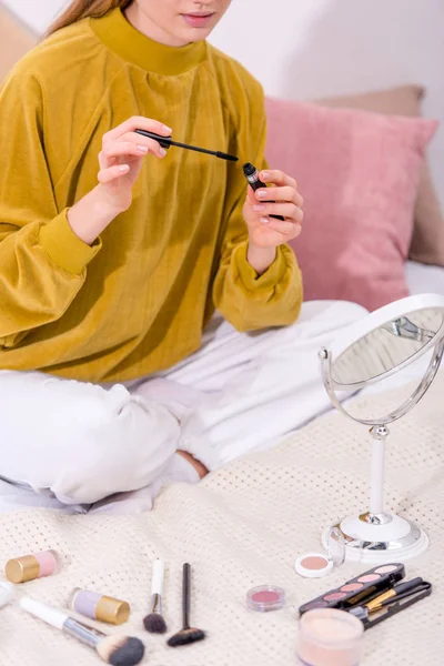 Plan recadré de jeune femme appliquant mascara tout en étant assis sur le lit à la maison — Photo de stock