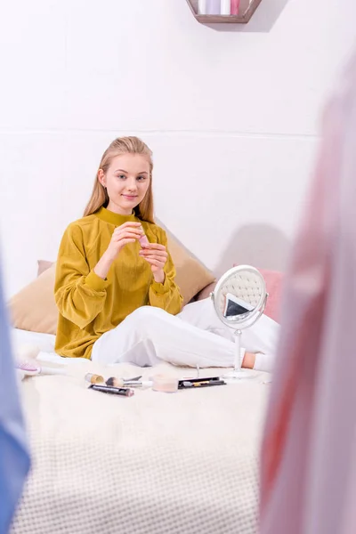 Junge Frau schminkt sich, während sie zu Hause auf dem Bett sitzt — Stockfoto