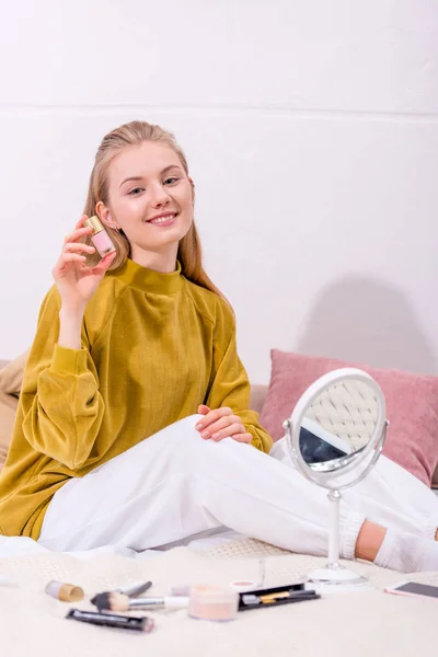 Jovem com frasco de esmalte de unhas sentado na cama em casa — Fotografia de Stock