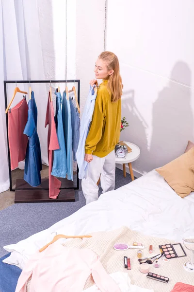 Vue grand angle de la jeune femme souriante choisir des vêtements à porter dans la chambre — Photo de stock