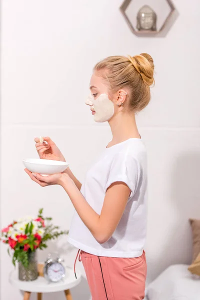 Side view of young woman applying clay mask on face at home — Stock Photo