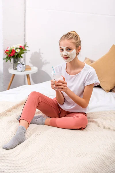 Hermosa mujer joven con máscara facial de arcilla blanca con batido en tarro de albañil en casa - foto de stock