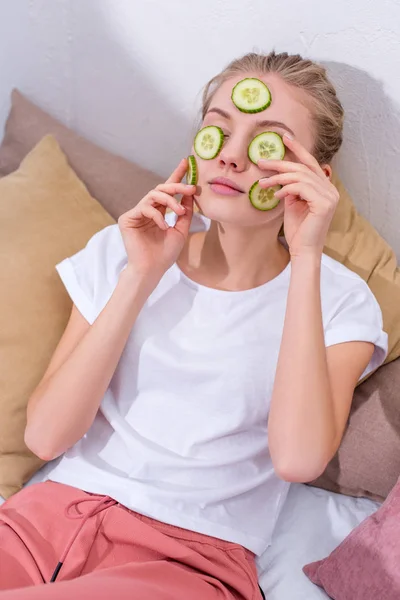 Vista ad alto angolo di giovane donna che applica fette di cetriolo sul viso a casa — Foto stock