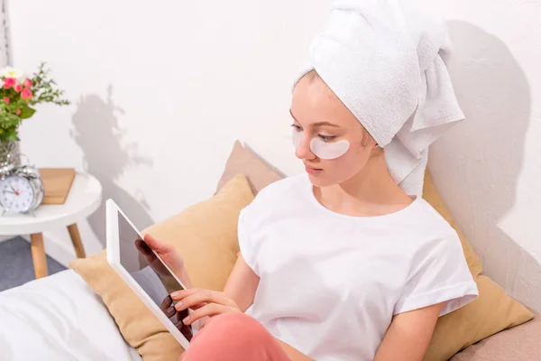 Молодая женщина с косметическими нашивками на лице с помощью планшета дома — стоковое фото
