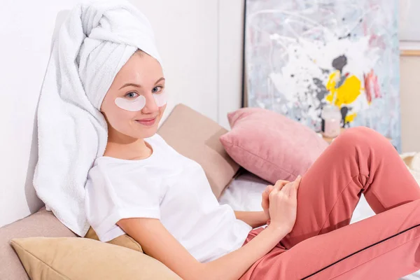 Mujer joven con parches faciales cosméticos relajándose en la cama en casa - foto de stock