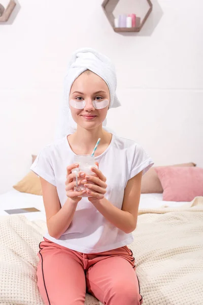 Привлекательная молодая женщина с косметическими нашивками для лица и стаканом молочного коктейля дома — стоковое фото