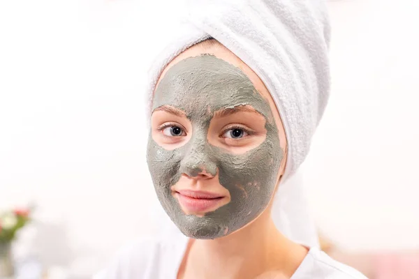 Beautiful young woman with cosmetic clay mask at home — Stock Photo