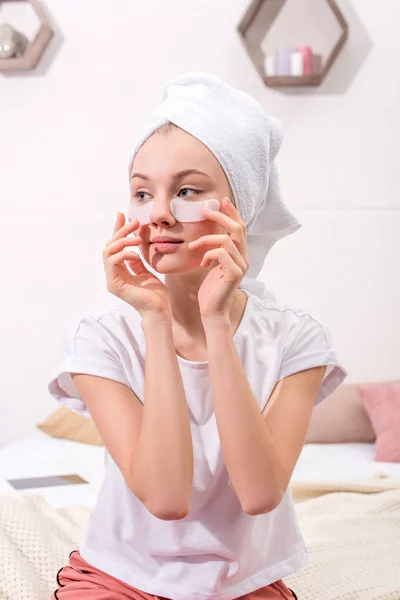 Mujer atractiva espiando parches faciales cosméticos en casa - foto de stock