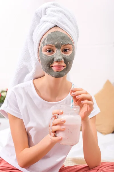 Jovem mulher com máscara de barro cosmético beber milkshake em casa — Fotografia de Stock
