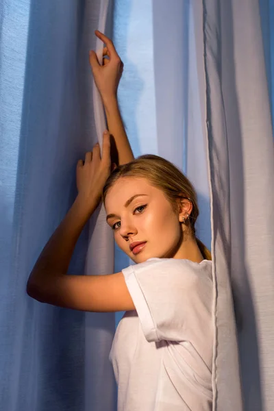 Belle jeune femme appuyée sur la fenêtre avec des rideaux blancs — Photo de stock