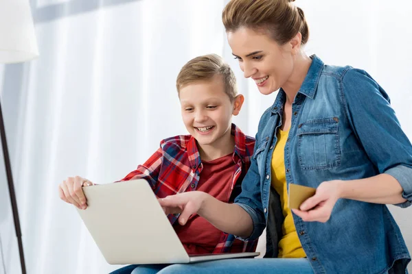 Hermosa madre e hijo haciendo e-shopping con laptop y tarjeta de crédito - foto de stock