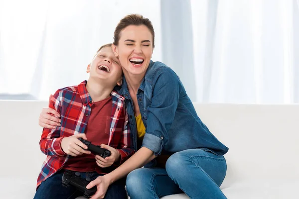 Mère heureuse embrassant fils tout en jouant à des jeux vidéo ensemble — Photo de stock