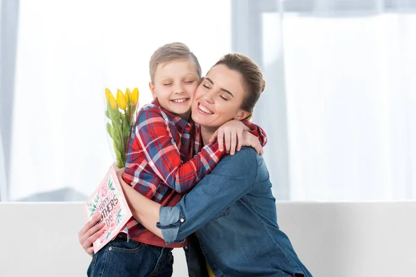 Sonriente madre e hijo abrazando en madres día después de que él le dio flores - foto de stock