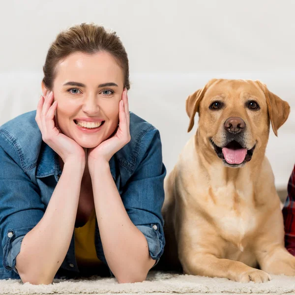 Mujer feliz con su perro labrador tumbado en el suelo en casa y mirando a la cámara - foto de stock