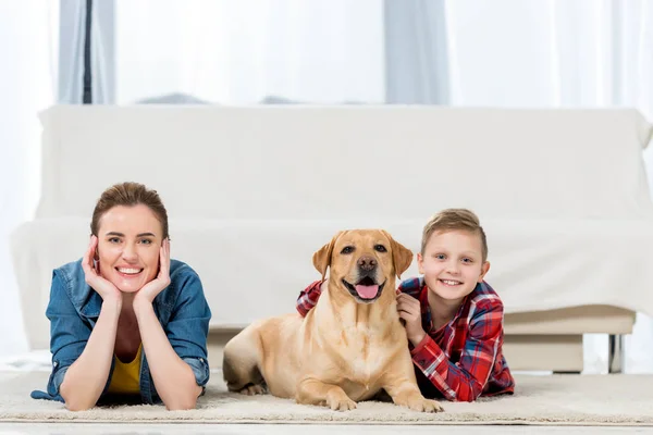 Hermosa madre e hijo tumbado en el suelo con su perro y mirando a la cámara - foto de stock