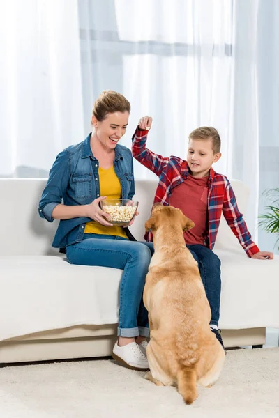 Madre e hijo alimentando a su perro con palomitas de maíz mientras él está sentado en el suelo - foto de stock