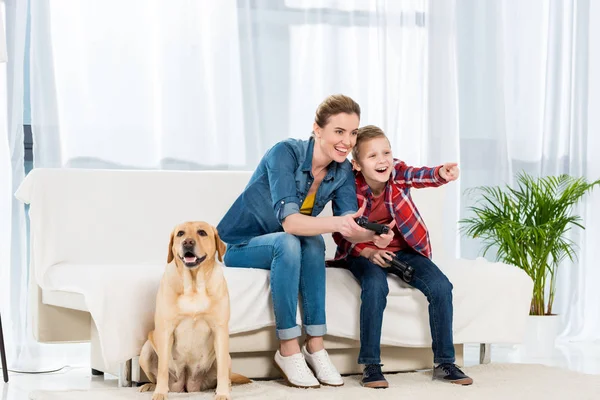 Mutter und aufgeregter Sohn spielen Videospiele, während ihr Hund auf dem Boden sitzt — Stockfoto