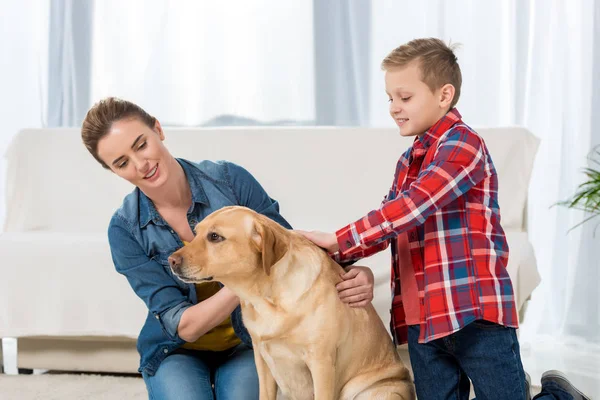 Mãe e filho acariciando seu cão labrador amarelo — Fotografia de Stock