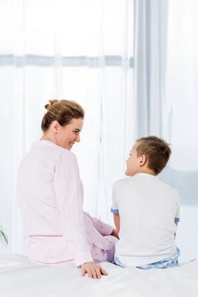 Rear view of mother and son sitting on bed together in morning — Stock Photo
