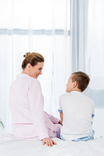 Vista trasera de la madre y el hijo sentados en la cama juntos en la mañana - foto de stock