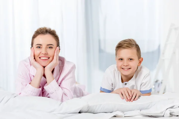 Madre e hijo acostados en la cama en pijama y mirando a la cámara - foto de stock