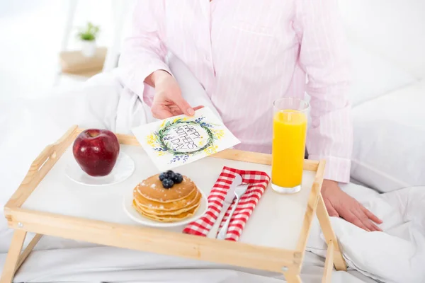 Plan recadré de femme avec petit déjeuner au lit et carte de vœux de la fête des mères — Photo de stock