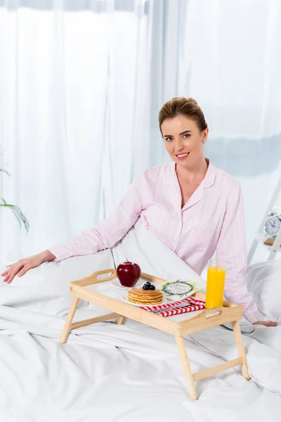 Mujer feliz en pijama con desayuno en la cama - foto de stock