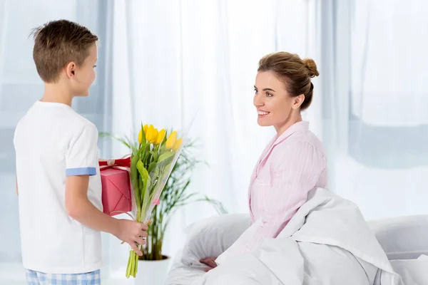 Son holding gift and flowers for happy beautiful mother on mothers day morning — Stock Photo