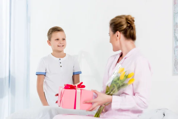Mutter mit Geschenk und Blumenstrauß, überreicht vom kleinen Sohn am Muttertagmorgen — Stockfoto
