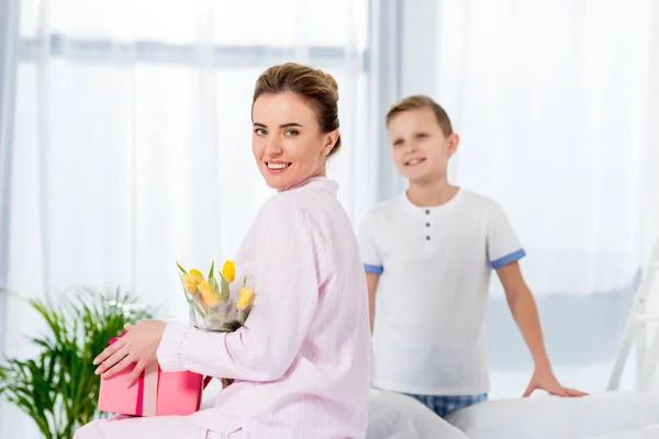 Mutter mit Geschenk und Blumenstrauß, überreicht vom Sohn am Muttertagmorgen — Stockfoto