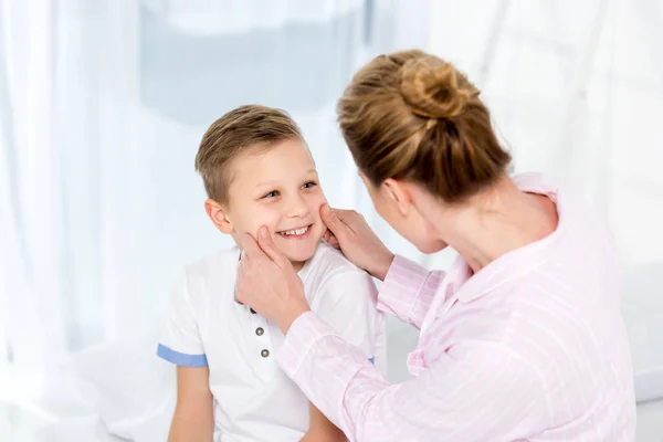 Mother tweaking cheeks of little son in bed in morning — Stock Photo