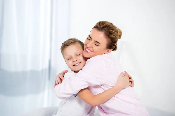 Madre e hijo en pijama abrazándose en la mañana - foto de stock