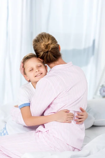 Madre e figlio in pigiama abbracciati al mattino seduti a letto — Foto stock