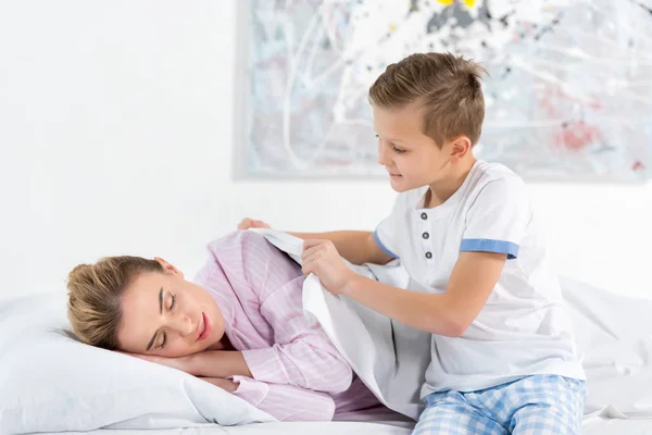 Маленький сын покрывает свою спящую мать одеялом — стоковое фото