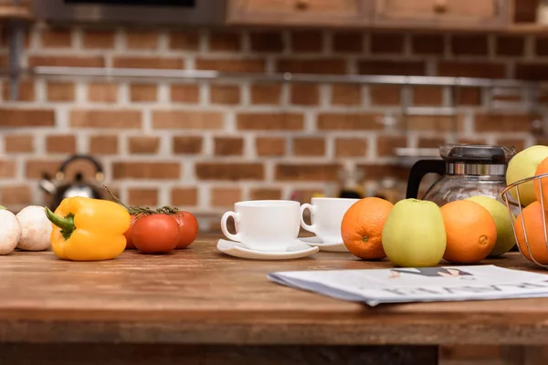 Tazas con café y verduras con frutas en la mesa - foto de stock