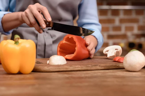 Woman cutting red bell pepper on wooden board — Stock Photo