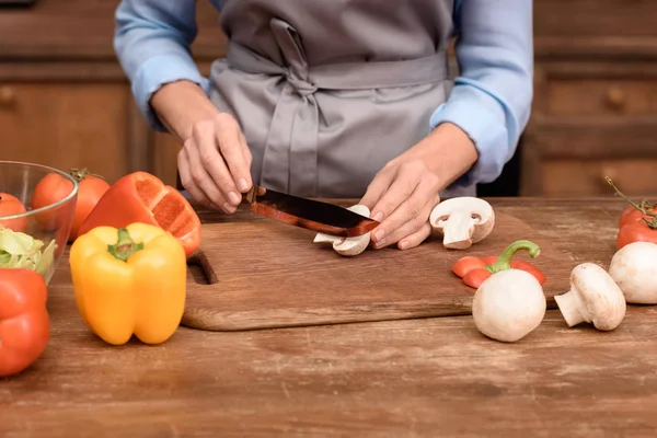 Cropped image of woman cutting mushrooms on wooden board — Stock Photo