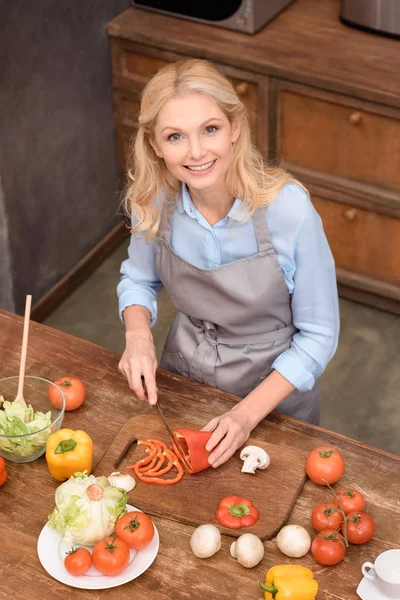 Vue grand angle de femme coupant des légumes et regardant la caméra — Photo de stock