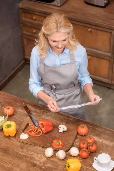 Vista ad alto angolo di donna che legge il giornale in cucina — Foto stock