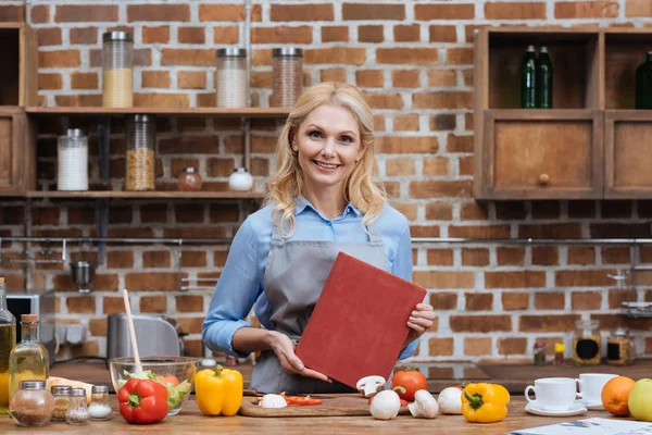 Mulher segurando livro de receitas na cozinha — Fotografia de Stock