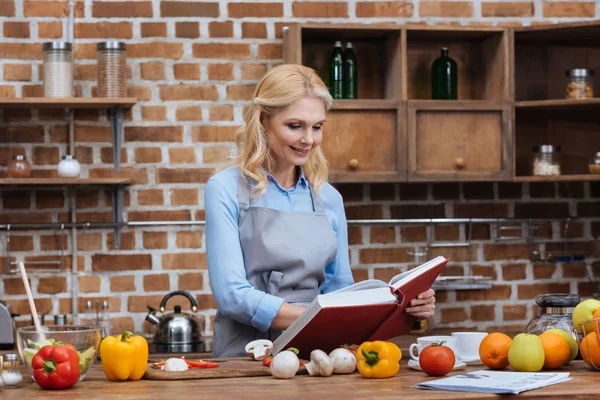 Женщина читает рецепт книги на кухне — стоковое фото