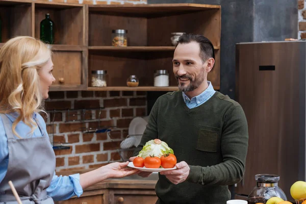 Wife giving plate with vegetables to husband — Stock Photo