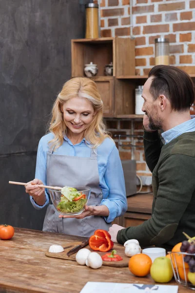 Улыбающаяся жена смешивает салат на кухне — стоковое фото